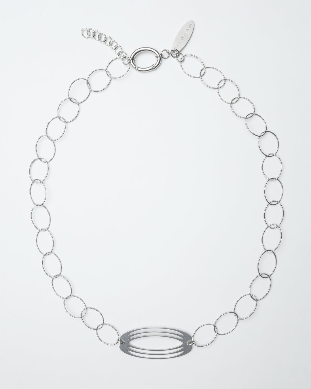 A silver-colored unisex belt with a laser-cut pendant, logo tag, and oval hook, worn around the waist.